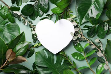 Tropical nature background with green leaves and white heart shaped paper for copy space. Top view....