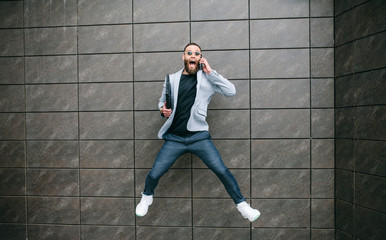 Positive handsome young businessman running in the air along an empty wall. Crazy emotions.