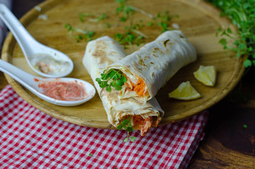 Shaurma, burrito, chicken roll in a pita with fresh vegetables and cream sauce on dark wooden background.
