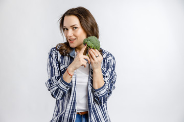 Young beautiful girl in plaid shirt holding broccoli on white background. Healthy food - vegetables, fruits and berries.