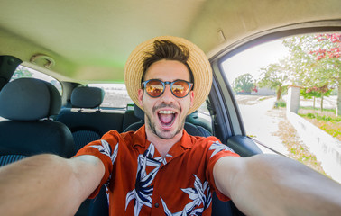 Happy young driver taking a selfie on his rental car at vacation