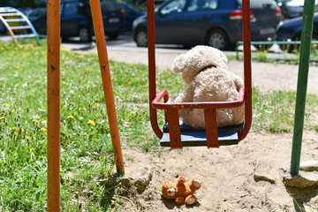 Danger of falling child, teddy bear fell to the ground from an old swing