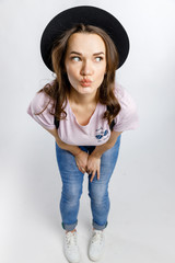Young beautiful girl posing in stylish black hat on white background. Emotions and gestures.