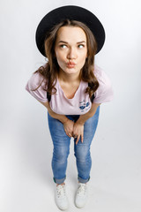 Young beautiful girl posing in stylish black hat on white background. Emotions and gestures.