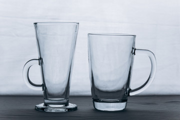 a pair of empty transparent glass glasses on a gray silver background close-up. two tall mugs with a handle and a leg. copy space, texture, background