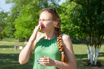 Fototapeta premium Young woman with allergy during sunny day is wiping her nose.