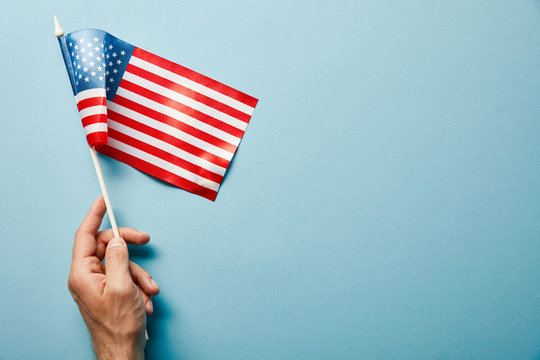 cropped view of man holding american flag on stick on blue background with copy space