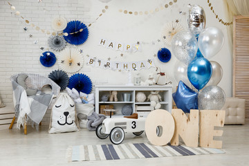 Birthday decorations with gifts, toys, garlands and figure for little baby party on a white bricks background. 