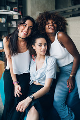 three young multiracial women posing together and looking camera