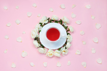 Obraz na płótnie Canvas Upper sight of a cup of tea surrounded by cute white rose and their petals on pastel pink background. Close Up of cup of tea. Flat lay.