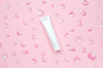 White glossy plastic tube with flower petals for medicine or cosmetics, cream, gel, skin care, toothpaste on pastel pink background.