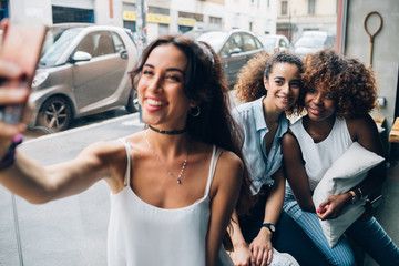 three young multiracial women using smartphone and posing together