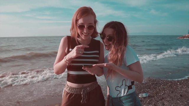 Best friend girls are looking smartphone, shocking and smiling, laughing on beach. Social media and summer concept. 