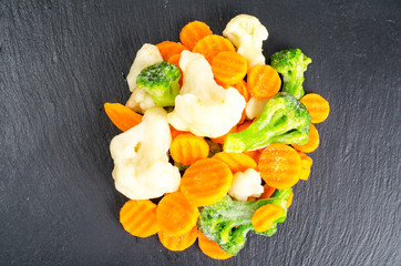 Mix of frozen vegetables on black stone background