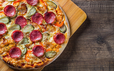 Pepperoni Pizza with Mozzarella cheese, salami, bacon, Tomato sauce, pepper, Spices and pickled cucumbers. Italian pizza on wooden table background