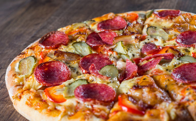 Pepperoni Pizza with Mozzarella cheese, salami, bacon, Tomato sauce, pepper, Spices and pickled cucumbers. Italian pizza on wooden table background