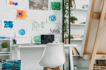 selective focus of spacious room with paintings on wall and rack with plants