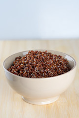 Cooked prep red quinoa in a bowl on a wooden background.