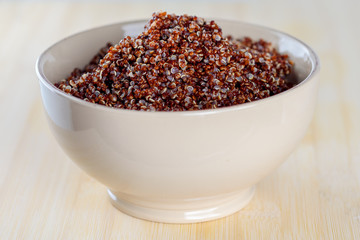 Red quinoa in a bowl on a wooden background.