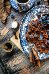 Overhead shot of homemade yummy chocolate waffles on vintage plates with blue ornament stands on wooden dark table