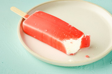 ice cream. Homemade red glaze  ice cream on a stick in white bowl on a turquoise background. Top view. Sweet dessert closeup