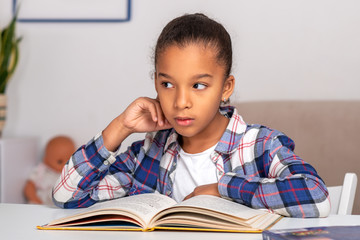 The schoolgirl sits at the table indoors and does his homework.