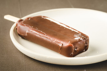 ice cream. Homemade dark chocolate ice cream on a stick in white bowl. Dark background. Sweet dessert closeup
