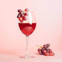 A glass with red wine and a bunch of grapes on a gentle pink background. Selective focus. Copy space. Minimalism.