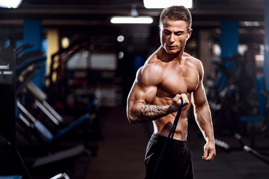 Pushing Hard Sportsman Working Out With Resistance Band Over Dark