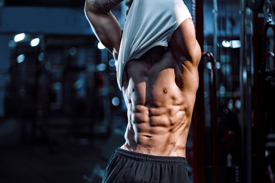 Side view of a caucasian handsome fitness model posing in the gym. Man on diet flexing muscles and six pack abs