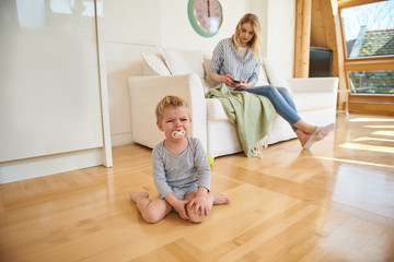 Upset little boy crying while his mother using cellphone