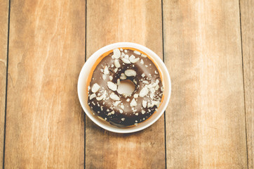 Donat in chocolate glaze in a white bowl on a wooden background. Top view