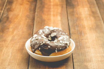 Donat in chocolate glaze is strewed with almonds. Wooden background.