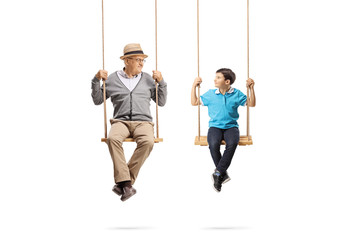 Senior man and boy sitting on swings and looking at each other