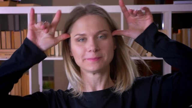 Closeup shoot of young attractive female student making funny facial expressions looking at camera indoors in the university library