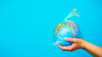 Woman holds in hands plastic bag with planet earth at blue background. The concept of plastic...