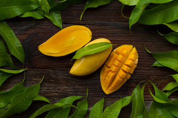 Mango fruit with green tropical leaves on wooden background.