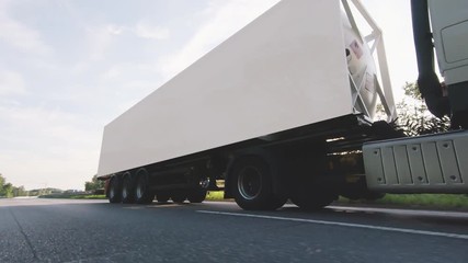 Cargo truck with cargo trailer driving on a highway. White Truck delivers goods in early hours of the Morning - very low angle drive thru close up shot.