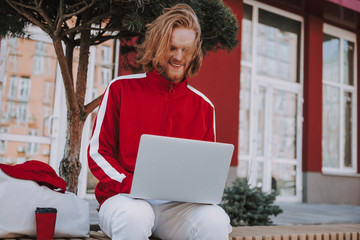Smiling hipster man working on laptop outdoor