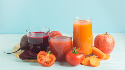 Fresh juice smoothies from a variety of vegetables beetroot apple carrot tomatoes in glasses on wooden blue background.