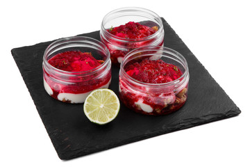 Raspberry cheesecake dessert in a jar on a black stone plate on a white background