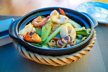 Fried seafood with noodles and fresh vegetables in bowl on table in restaurant