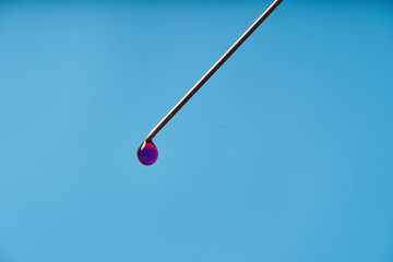 A drop of medicine on the tip of a medical injection needle. Blue background