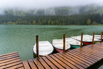 Small boats floating on wooden pier on a calm lake. Smooth calm surface of mountain lake. Mountain...