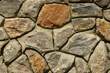 Part of the wall. Masonry of stone and cement. Multicolored large cobbles in sunlight