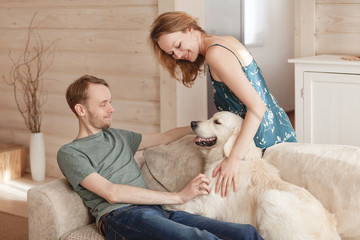 Happy family couple young girl and cute guy spends time sitting with his beloved dog in the cozy room of his country house