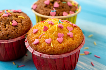 Delicious homemade colorful cupcakes with heart-shaped confectionery close up on a light blue wooden background