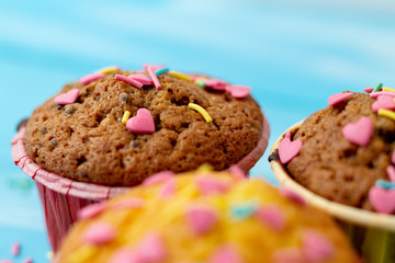 Delicious homemade colorful cupcakes with heart-shaped confectionery close up on a light blue wooden background
