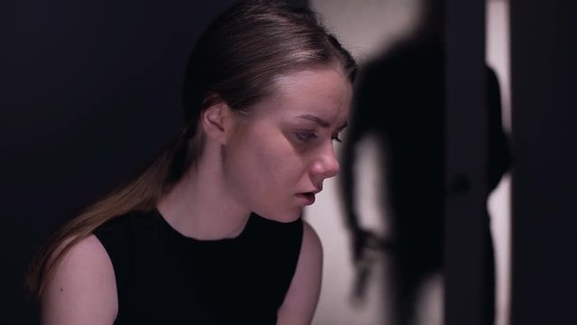 Crying terrified female looking at drunkard husband silhouette entering room