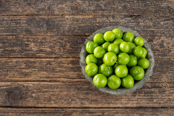 Many isolated green sour plums in a bowl on the rustic wooden table